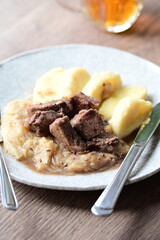 Traditional Czech dish of roasted wild boar with sauerkraut and dumplings, served on a plate in a cozy home-style setting. A hearty and flavorful meal representing authentic Czech cuisine and rustic c