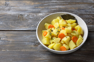 Rustic homemade stew with tender potatoes and carrots served in a ceramic bowl on wooden table. Warm comfort food with herbs and spices, natural light and cozy texture