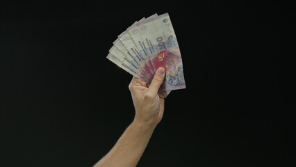 Hand of a caucasian man holding argentine pesos banknotes against black background, showcasing...