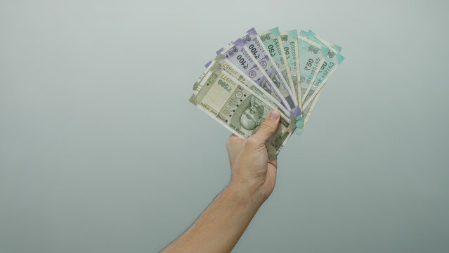 Caucasian man holding indian rupee banknotes against a white background, symbolizing currency and finance with hand prominently displaying modern indian money notes.