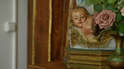 Fototapeta premium Cherubic sculpture adorned with roses in an ornate vase against a church's wooden wall captures a tranquil and sacred indoor ambiance.