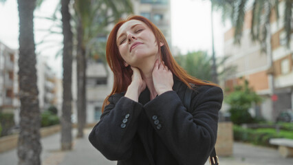 Woman experiencing neck pain on a city street wearing black coat outdoors provides an urban...