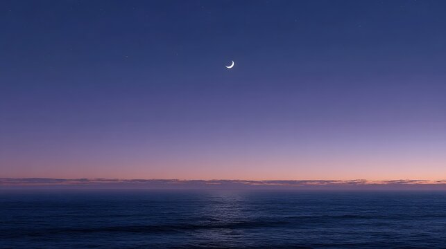 A crescent moon shines in the twilight sky above a calm ocean horizon