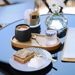 Cup of espresso with sparkling water and dessert served on an elegant outdoor café table. Minimalist presentation of coffee break during inflation and rising café prices.