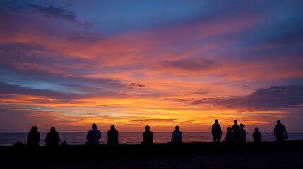 A silhouetted group of people contemplate a vividly colorful sunset over the ocean creating a serene evening scene