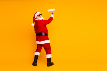 Santa paints a bright wall with a roller in a red suit hat and boots for Christmas season creating a festive playful moment