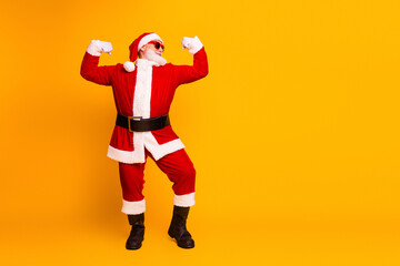 Happy Santa in red suit strikes a bold flex pose in a bright yellow studio for festive Christmas season