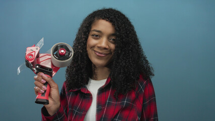 Woman holding red tape dispenser in studio with blue background; productivity organization...