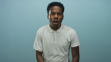 Young african american man with open mouth and raised eyebrows in studio wearing white polo shirt...