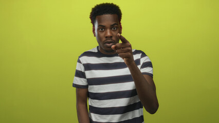 Young man pointing finger in studio wearing striped shirt with serious gaze; seriousness assertion intensity.