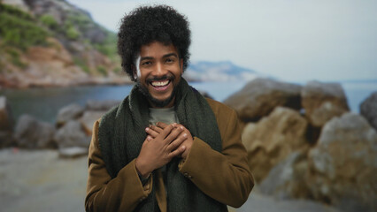 Smiling african american man on seaside beach with rocks in background enjoying peaceful outdoor setting under clear sky with ocean waves and distant mountains