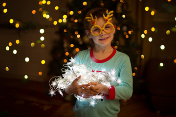 kid boy  Wearing carnival glasses with Christmas decor on near the Christmas tree at home. 