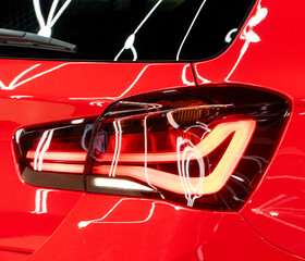 Naklejka premium Macro close up of a modern glowing LED tail light on a glossy red sports car body with bright white light reflections in a detailing studio.