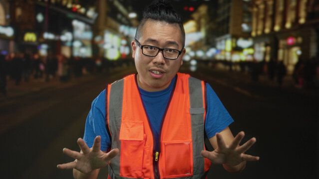 Man holding hands up palms out stop gesture on a city street at night wearing orange reflective vest; safety caution.