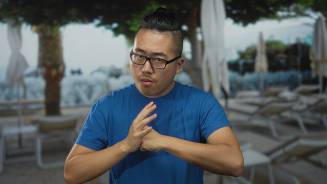 Man showing fists and blocking hand gesture on a street scene with umbrellas and poolside chairs; determination discipline courage.