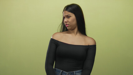 Naklejka premium Woman glances to side showing bare shoulder against green wall in studio under soft lighting; disgust.