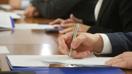 Close-up of businessman’s hand signing document with silver pen during meeting, concept of contract, resolution, or corporate agreement. Photo