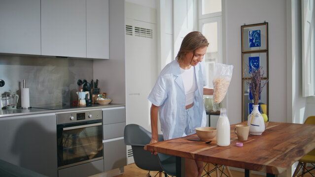 Pretty woman preparing breakfast in kitchen sunlight. Happy girl pouring cereal - Powered by Adobe