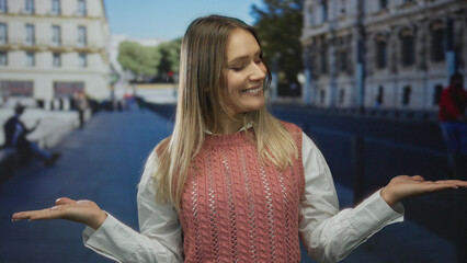 Woman smiling outdoors extends both hands as if weighing options against an urban city backdrop,...