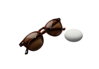 Stylish brown tortoiseshell round-frame sunglasses with dark brown tinted lenses and a pale grey river stone on a solid transparent background, high key studio lighting, luxury eyewear concept
