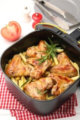 Grilled chicken wings with french fries and rosemary in air fryer basket on white wooden table, closeup