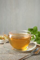 Tasty tea in glass cup and teaspoon on wooden table against grey background, closeup. Space for text