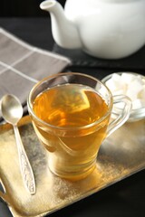 Tasty tea in glass cup, sugar cubes and teaspoon on black wooden table, closeup