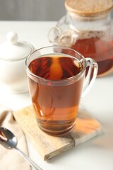 Tasty tea in glass cup and teaspoon on white table, closeup