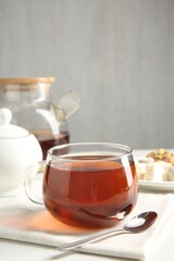 Tasty tea in glass cup and teaspoon on white table against grey background, closeup. Space for text