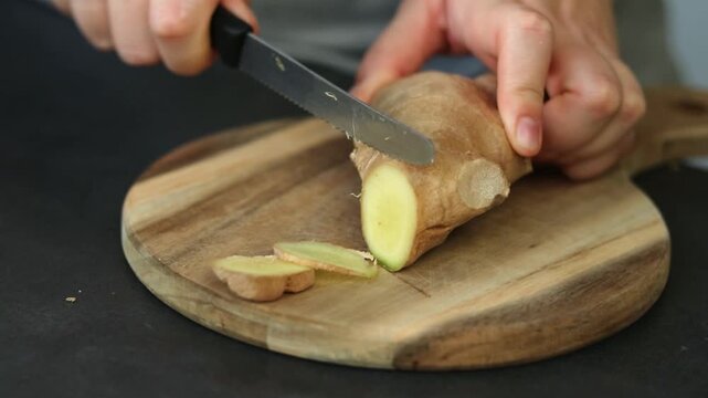 Close up of female hands cutting fresh ginger on wooden cutting board
