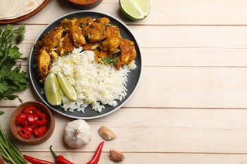 Delicious chicken tikka masala with rice, parsley, lime and spices on light wooden table, flat lay....