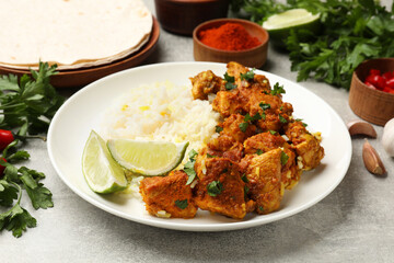 Delicious chicken tikka masala with rice, parsley and lime on grey textured table, closeup