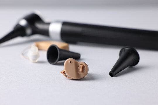 Modern otoscope, hearing aid and ear speculums on light grey background, closeup