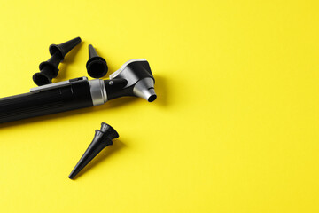 Hearing test. Modern otoscope and ear speculums on yellow background, closeup. Space for text