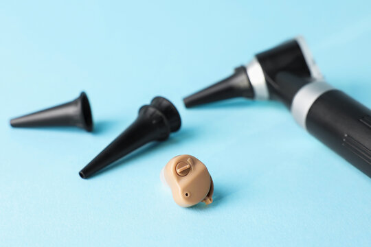 Modern otoscope, hearing aid and ear speculums on light blue background, closeup