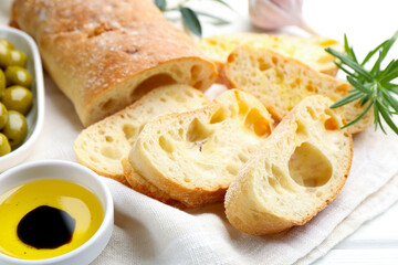 Fresh cut ciabatta, oil, olives and rosemary on white wooden table, closeup