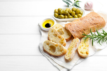 Fresh cut ciabatta, oil, olives, garlic and rosemary on white wooden table. Space for text