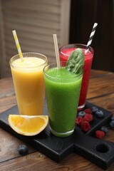 Different tasty smoothies in glasses and ingredients on wooden table, closeup
