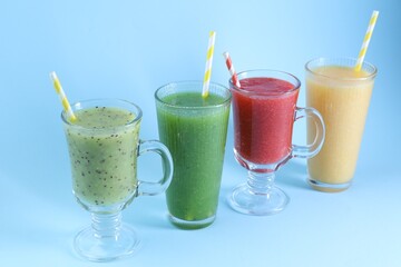 Different tasty smoothies in glasses on light blue background, closeup