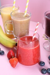 Different tasty smoothies in glasses and ingredients on pink background, closeup