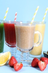 Different tasty smoothies in glasses and ingredients on light blue background, closeup