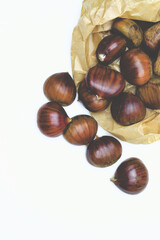 Close up of chestnuts on a white background and paper bag, zenith view. In vertical shot.