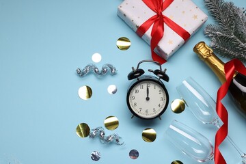 Alarm clock, bottle of sparkling wine, festive decor and gift box on light blue background, flat...