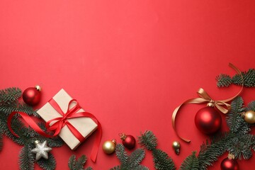 Fir tree branches, gift and Christmas decor on red background, flat lay. Space for text