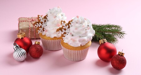 Tasty cupcakes with Christmas decor and gift box on pale pink background, closeup