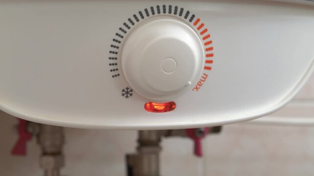 Regulator for heating cold water in boiler. Man turns temperature control on heater of water. Red light indicator comes off, boiler has turned off. Boiler heats water from cold water supply system