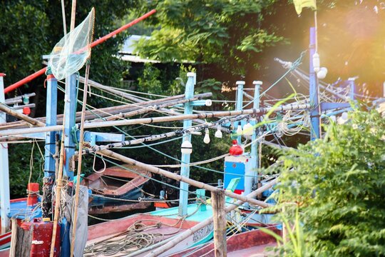 Traditional Thai fishing boats moored at a local pier in a coastal village. Authentic fisherman lifestyle featuring colorful wooden boats, fishing nets, and equipment under bright daylight. Scenic nau