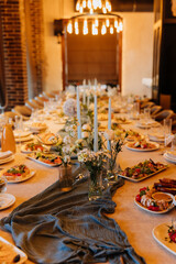 Long festive banquet table with candles, flowers and elegant appetizers in warm light