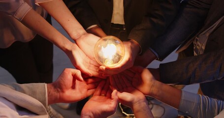 Top view of business people group putting their hands in s circle holding illuminated lightbulb sharing creative energy and innovative ideas. Teamwork, cooperation and success concept. 4l video. - Powered by Adobe