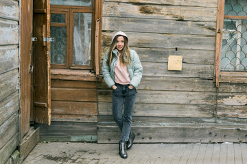 Woman in pastel jacket leaning on wooden wall outdoors. Calm mood, youth, and minimalism in vintage urban environment. Copy space.
